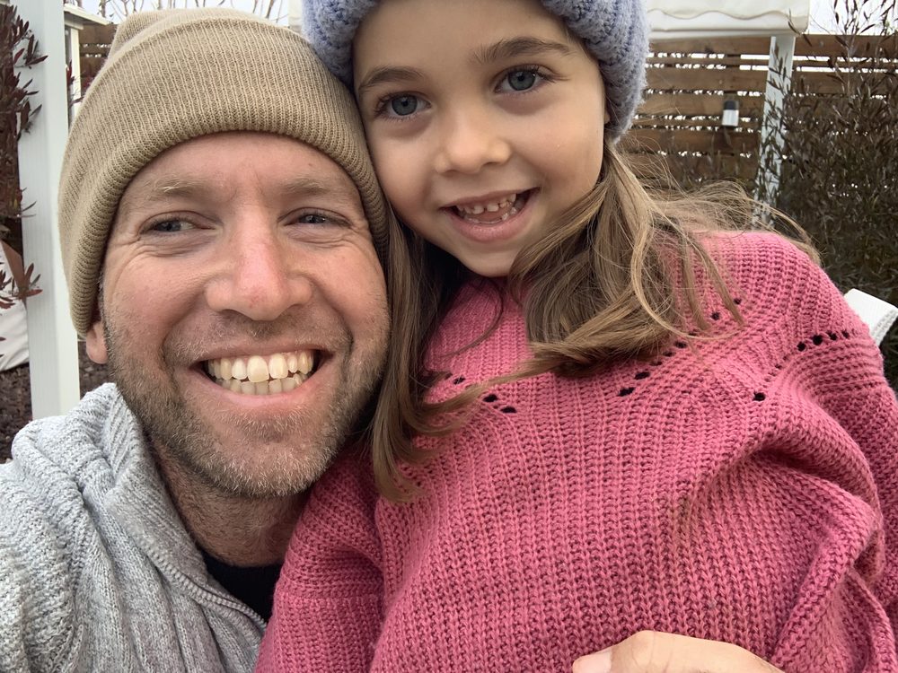 Tai cheek to cheek with his young daughter, both smiling, on a winter day at the farm